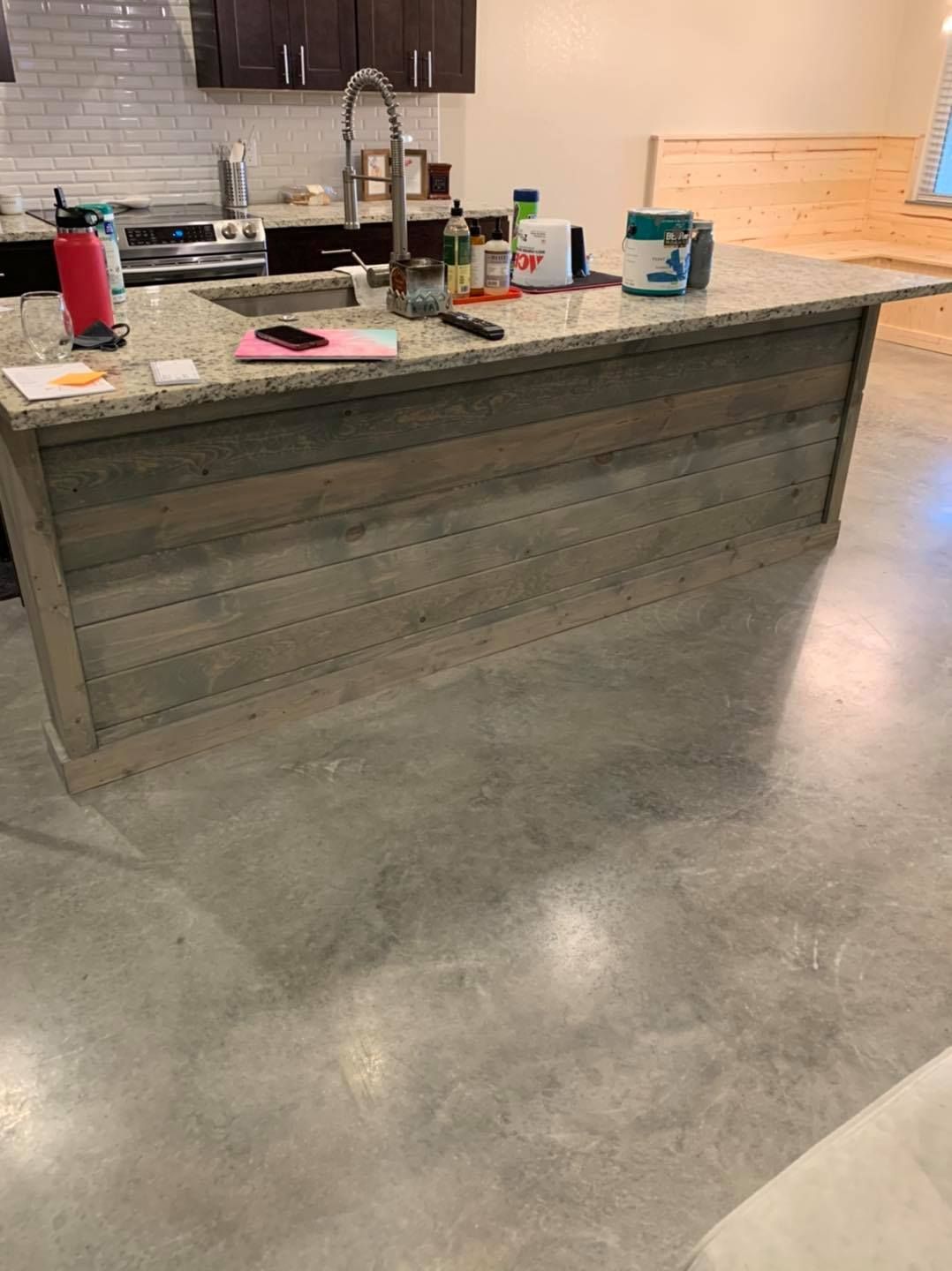 Kitchen island with a wooden facade, granite countertop, and concrete floor.