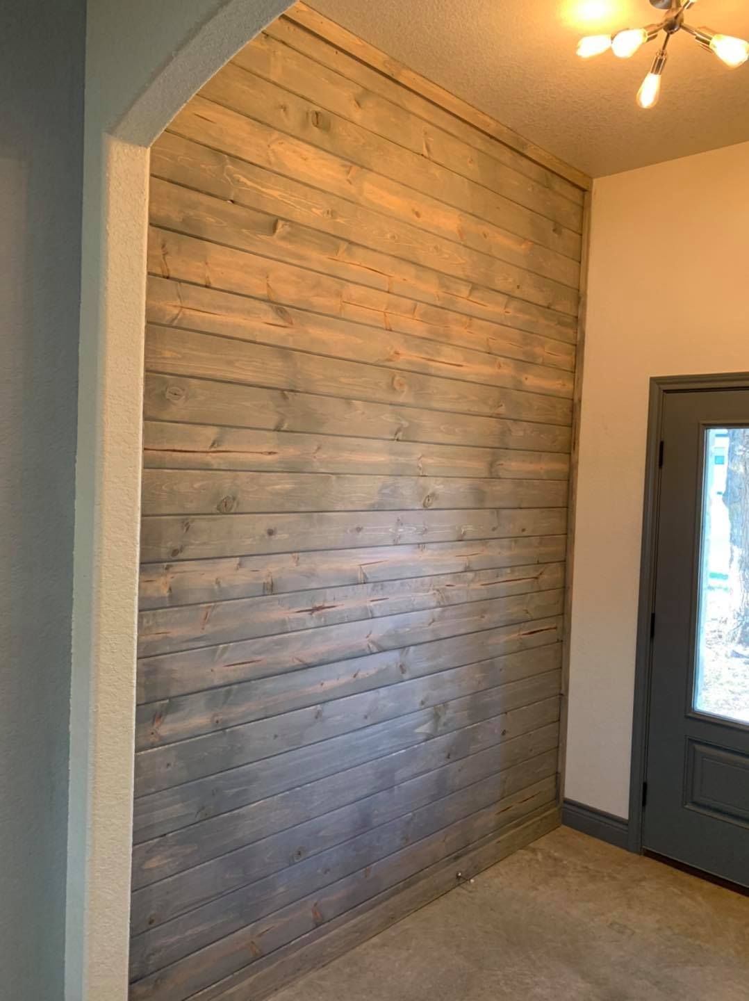 Wooden plank accent wall, grey and tan tones. Archway on the left, grey door on the right.