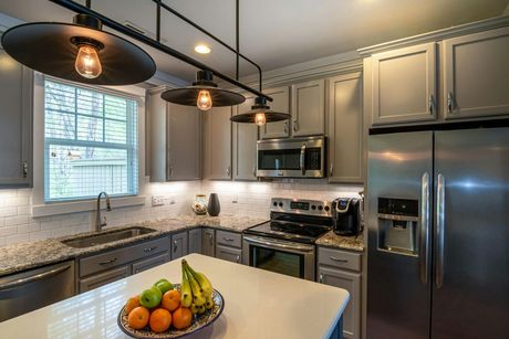 A modern kitchen featuring grey cabinets, granite countertops, stainless steel appliances, and hanging pendant lights.
