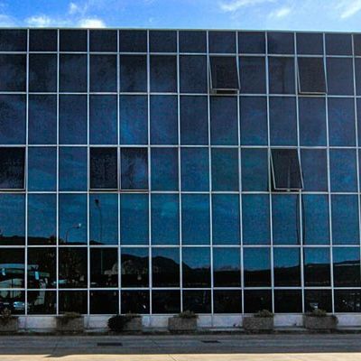 Edificio moderno con una griglia di finestre scure, alcune leggermente aperte, che riflettono il cielo e l'ambiente circostante.