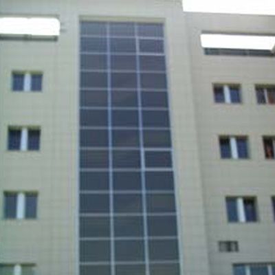 Esterno dell'edificio con una grande griglia di finestre rettangolari e diverse finestre più piccole. L'edificio è di colore beige chiaro.