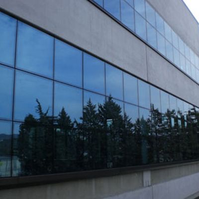 Le finestre blu riflettono gli alberi e il cielo sulla facciata di un edificio moderno.