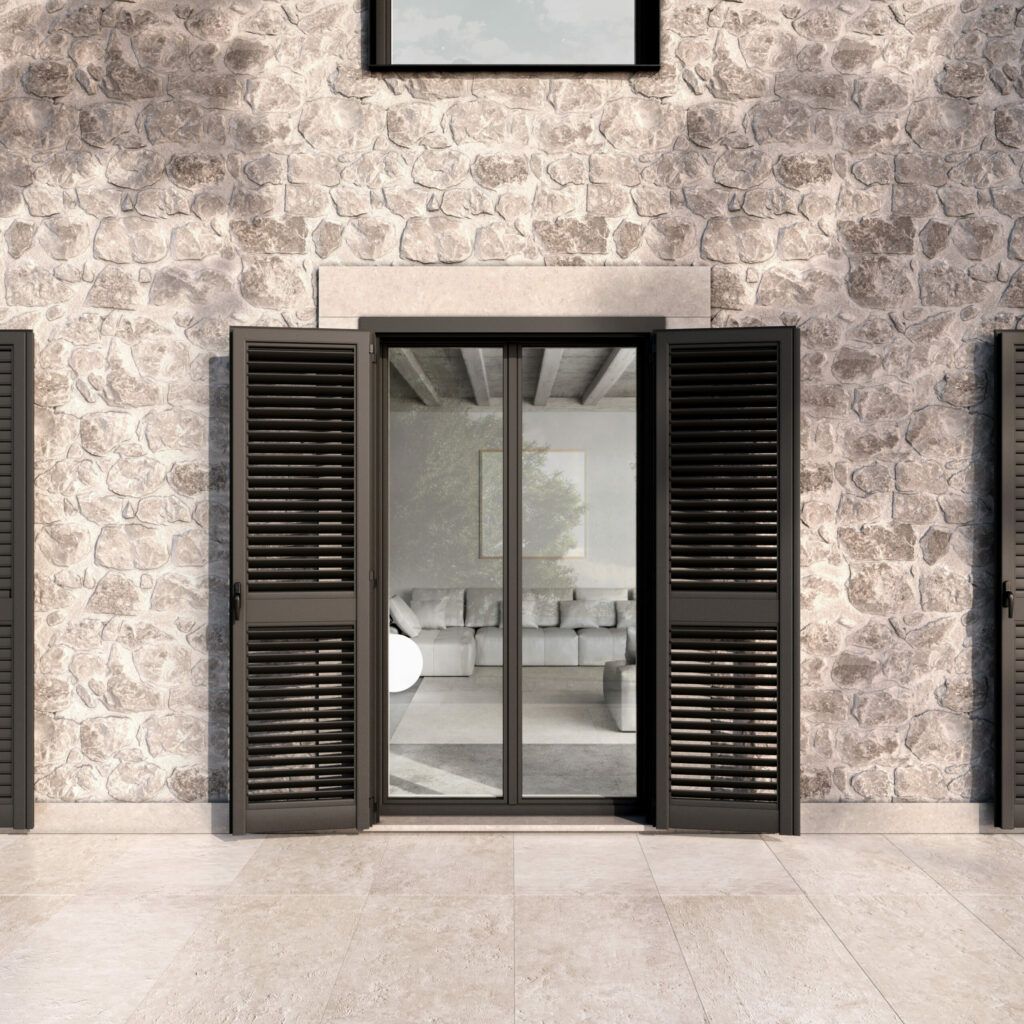 Esterno di un edificio con finestre con persiane aperte e una porta a vetri che conduce a un soggiorno; contro un muro di pietra.