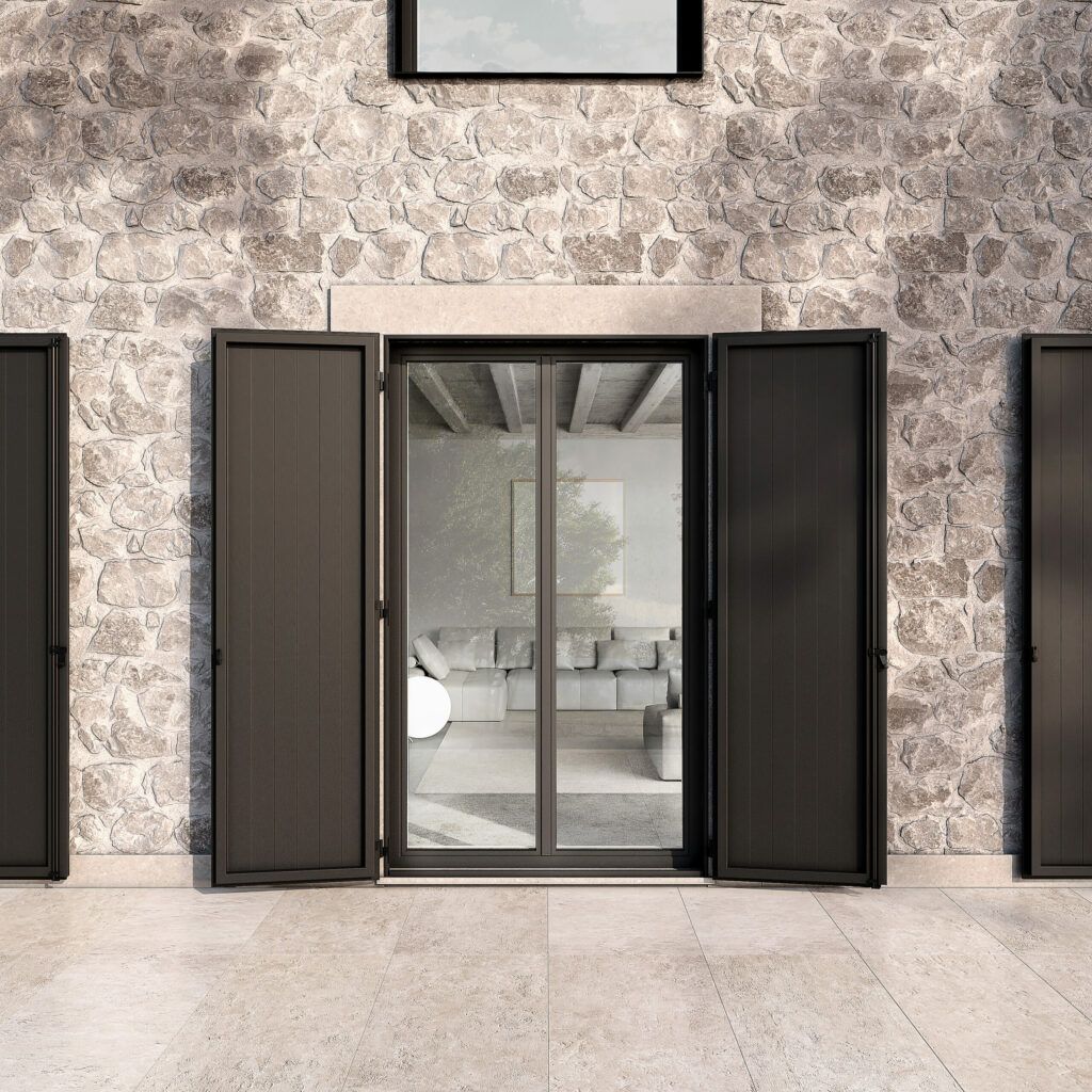 Persiane grigio scuro su un edificio con un muro in pietra e vista su un soggiorno moderno. Le persiane sono aperte intorno alla finestra.