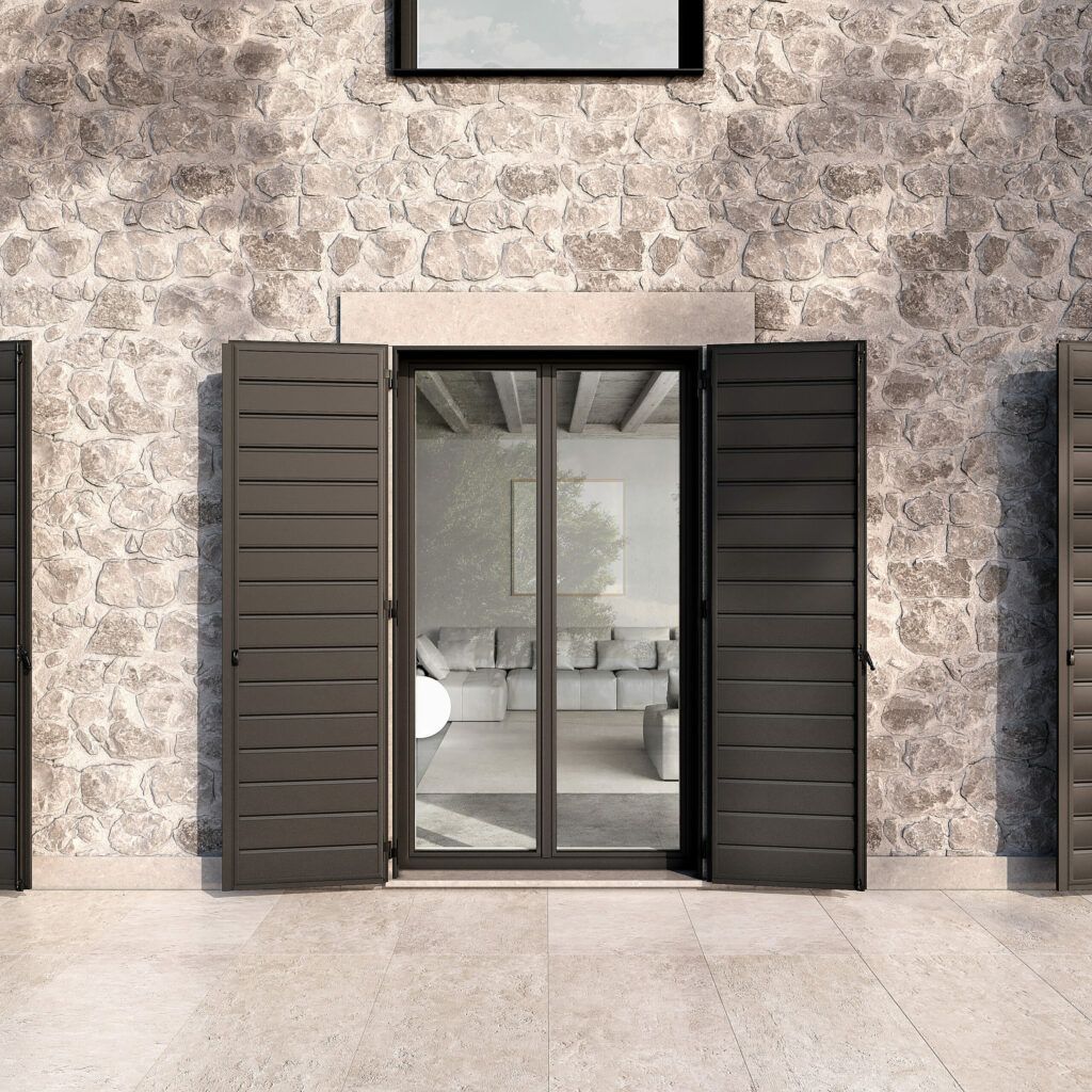 Esterno di un edificio in pietra con una porta a vetri fiancheggiata da persiane scure. Le persiane sono aperte.