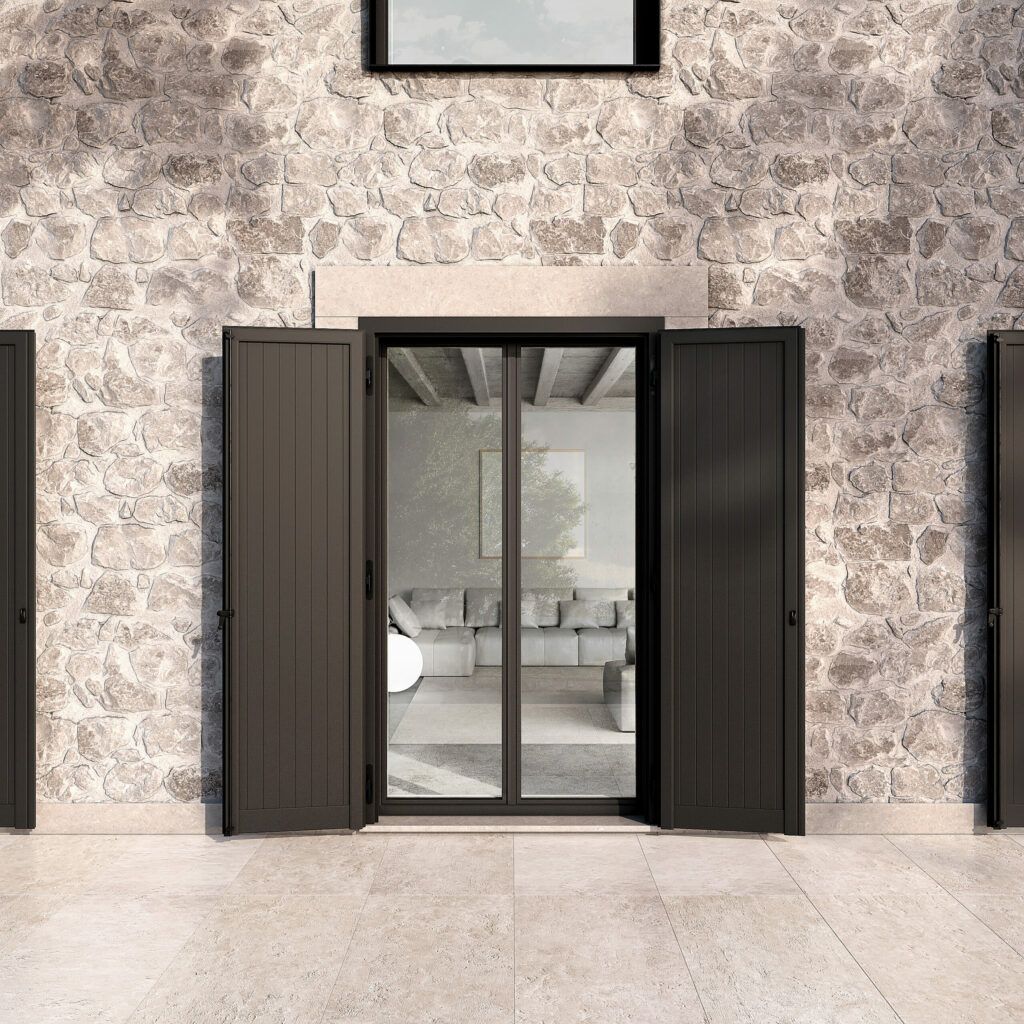 Un muro di pietra con una porta a vetri con cornice scura, fiancheggiata da persiane coordinate.