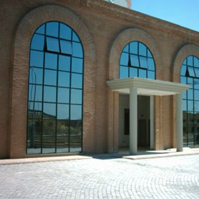 Un edificio con finestre ad arco e un ingresso di colore chiaro sotto un portico colonnato. L'esterno in mattoni è visibile.