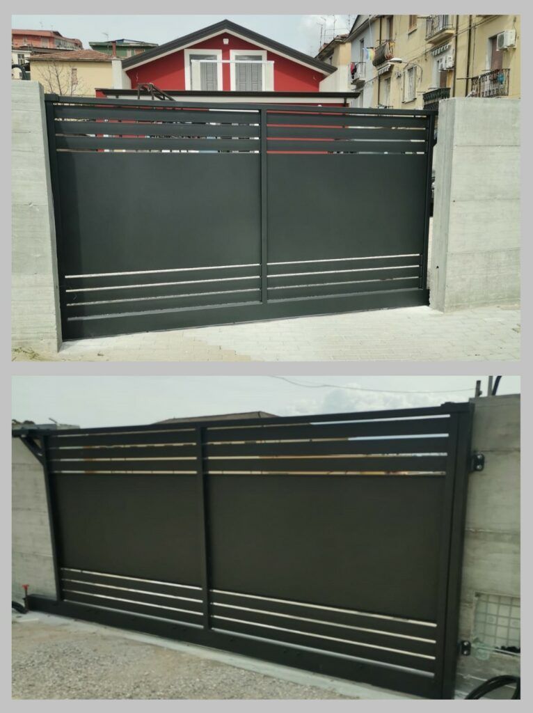 Cancello d'accesso in metallo nero con strisce orizzontali argentate, fiancheggiato da pilastri in cemento, posto di fronte a un edificio con il tetto rosso.