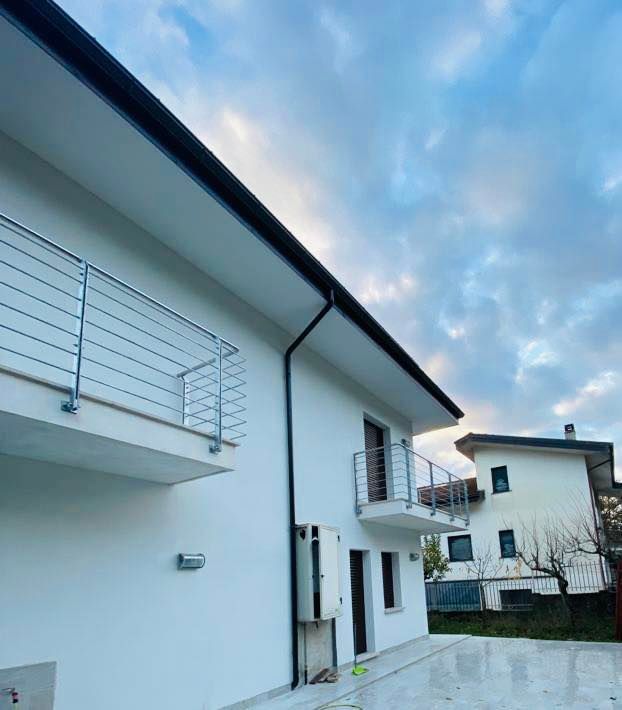 Casa bianca moderna con balconi, ringhiere in acciaio inox e cielo nuvoloso. Un'altra casa è visibile sullo sfondo.