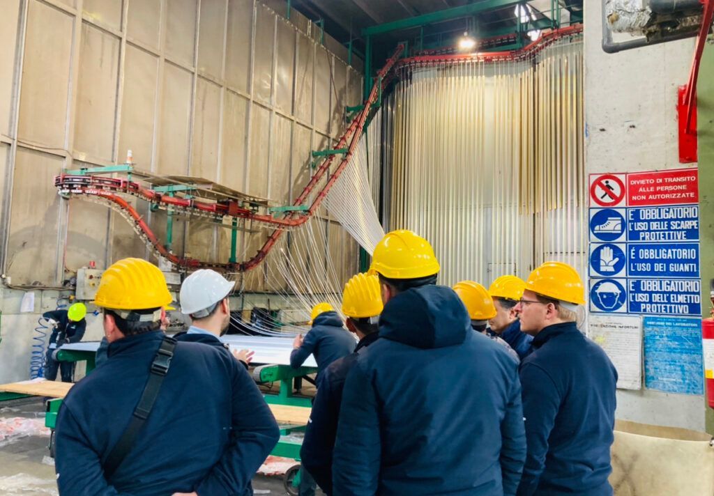 Un gruppo di persone con caschi gialli osserva un sistema di trasporto a forma di dinosauro all'interno di una fabbrica.