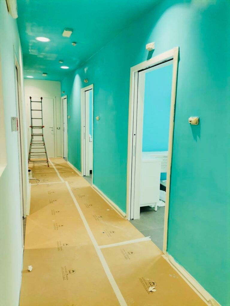 Un corridoio con pareti turchesi e porte bianche. Il pavimento, dove è posizionata una scala, è ricoperto di cartone.