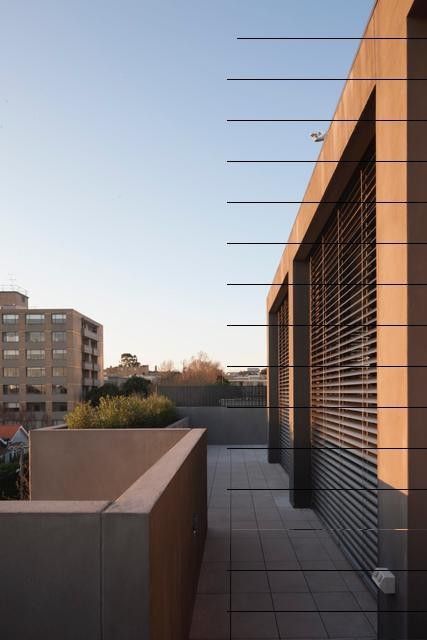 Vista esterna del tetto di un edificio moderno dai toni neutri. Una ringhiera lineare corre lungo il bordo e sullo sfondo si vedono altri edifici sotto un cielo terso.