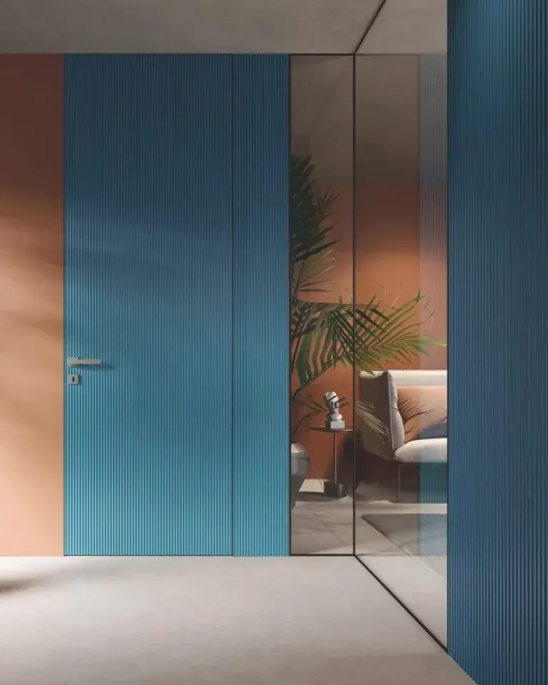 Porta in legno blu con maniglia minimalista, accanto a una parete in vetro che rivela uno spazio abitativo con pareti in terracotta.