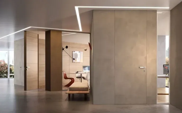Interni moderni con porte a filo e illuminazione minimalista. Toni neutri con scorcio di ufficio e luce naturale.