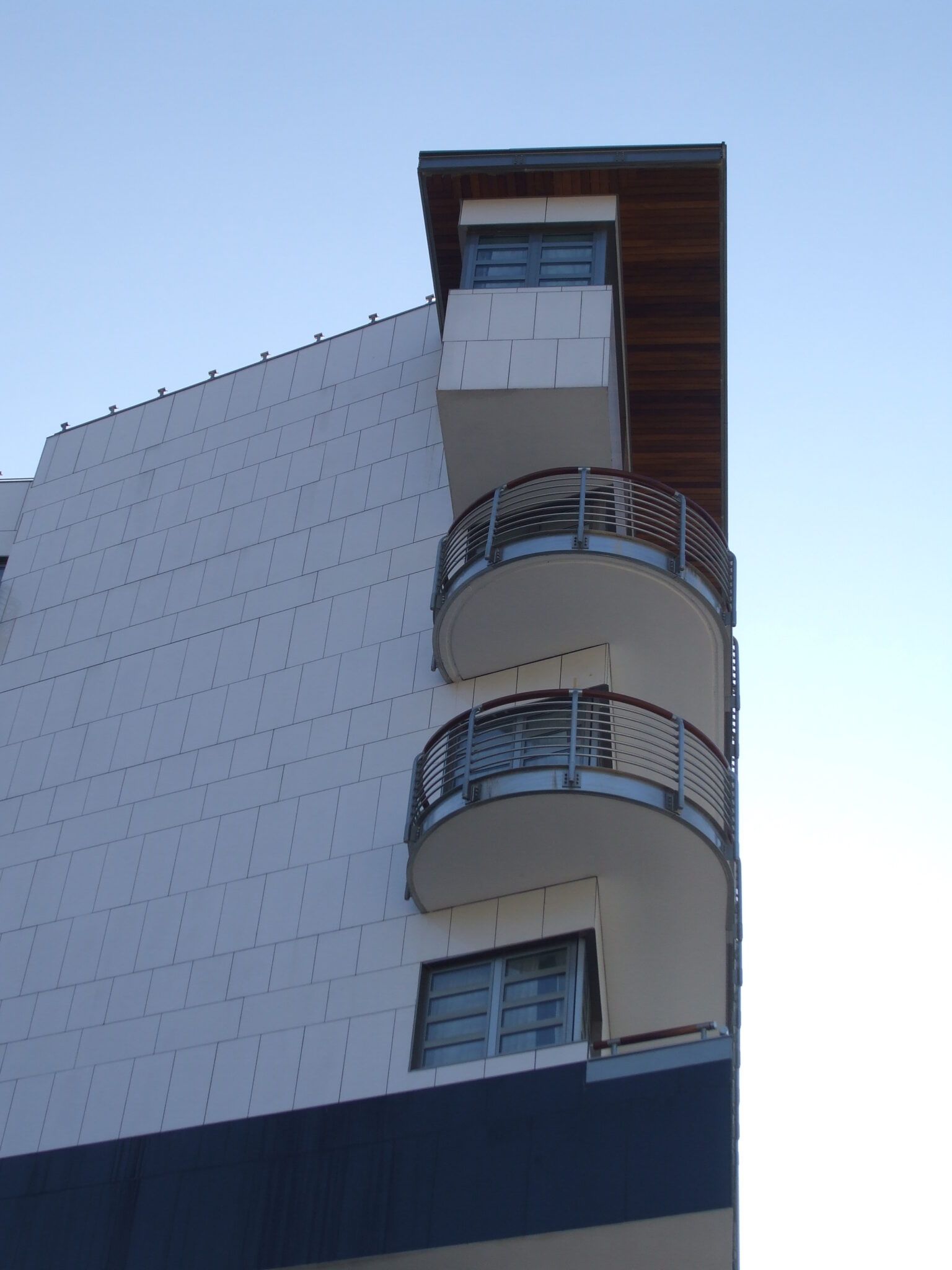Moderno edificio bianco con balconi curvi e accenti blu sullo sfondo di un cielo azzurro terso.