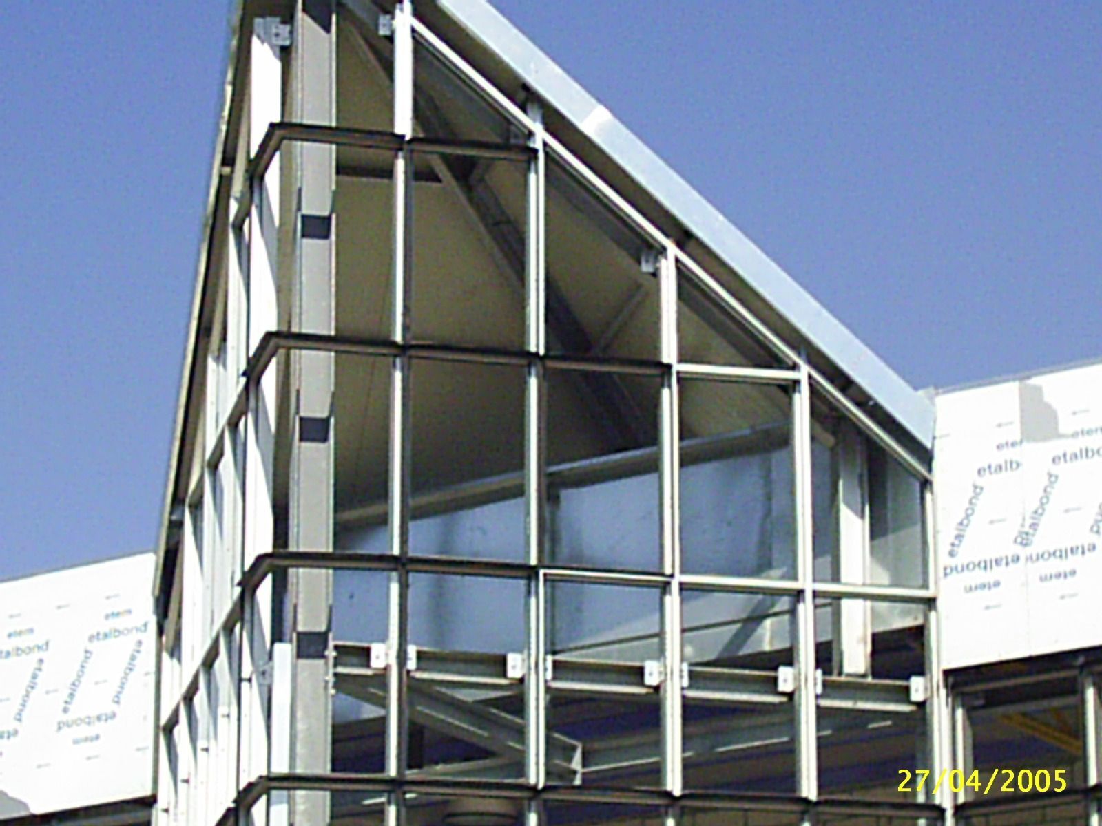 Vista esterna di un edificio moderno con una struttura del tetto triangolare in acciaio e vetro contro un cielo blu.