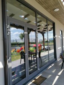 Le porte e le finestre in vetro con cornice grigia riflettono una scena esterna di prato, patio e cielo.