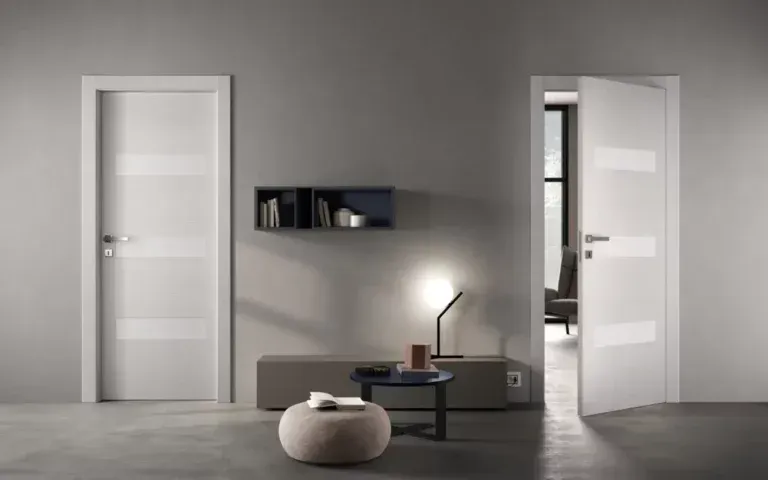 Due porte bianche, una aperta e una chiusa, in una moderna stanza grigia. Nella stanza sono presenti anche un tavolino, una lampada e un pouf.