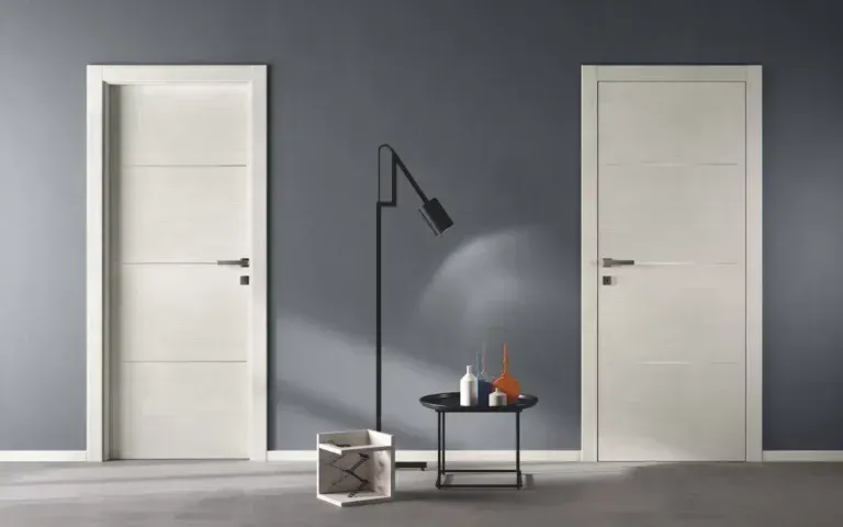 Due porte interne bianche fiancheggiano una parete grigio scuro. Tra di esse si trovano una lampada e un tavolino decorato.