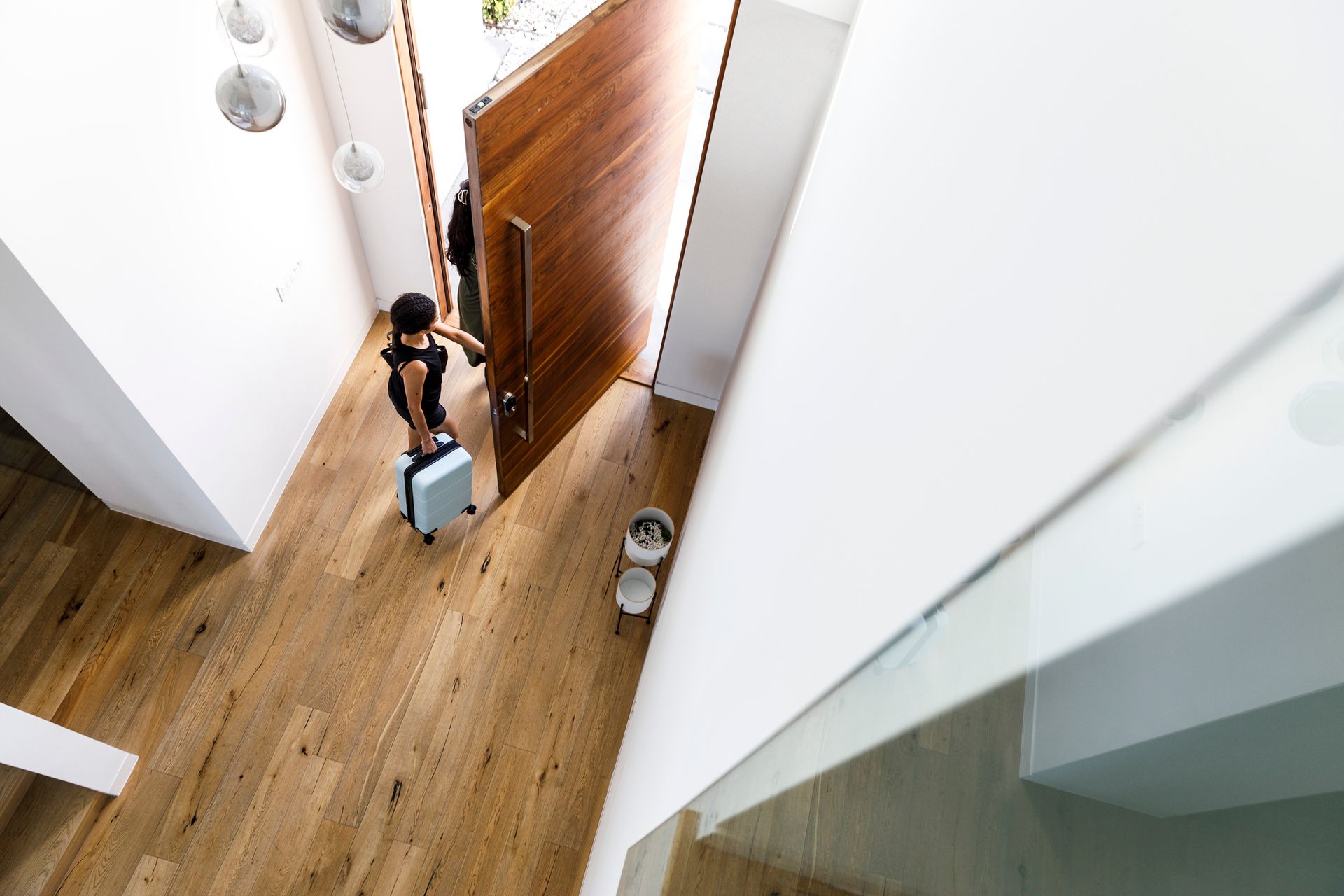 Persona che esce da una casa moderna con una valigia, pavimenti in legno e porta d'ingresso aperta.