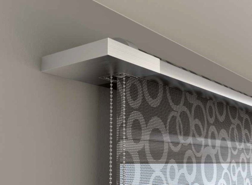Primo piano di una moderna tenda con architrave bianca e tende a motivi grigi e bianchi. La tenda è appesa a una parete grigio chiaro.