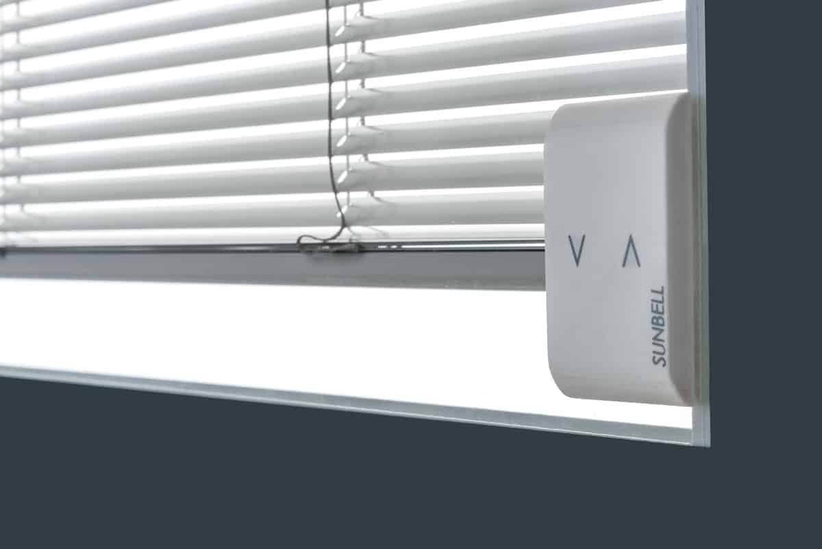 Un motore bianco intelligente per tende oscuranti fissato a una finestra con le tende chiuse. Il motore riporta la scritta 