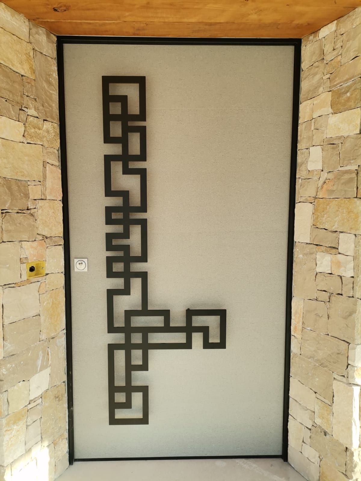 Porta d'ingresso moderna con motivo geometrico in metallo nero su vetro satinato, incorniciata da pareti in pietra.