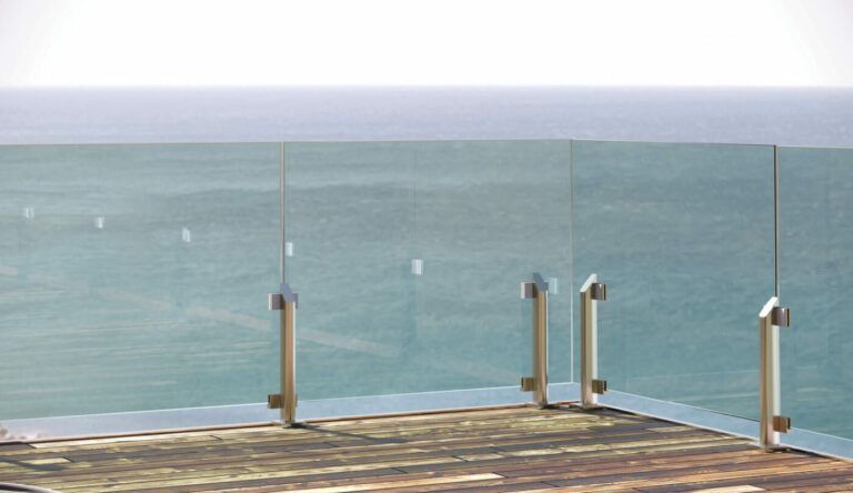 Ringhiera in vetro su una terrazza in legno con vista sull'oceano in una giornata luminosa e soleggiata.