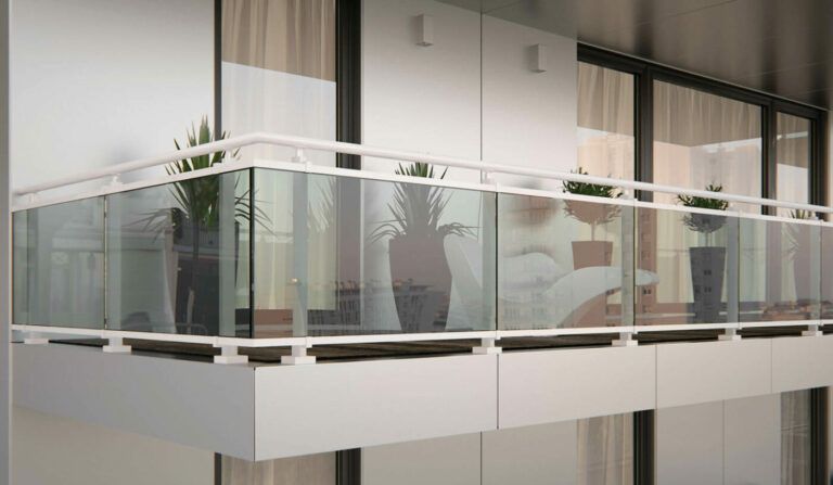 Balcone con ringhiera in vetro, cornice bianca e piante in vaso. Facciata bianca dell'edificio e ampie finestre visibili.