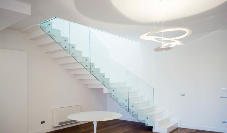 Scala bianca con ringhiera in vetro. Design moderno con pareti, soffitto e tavolo bianchi. Lampada a sospensione.