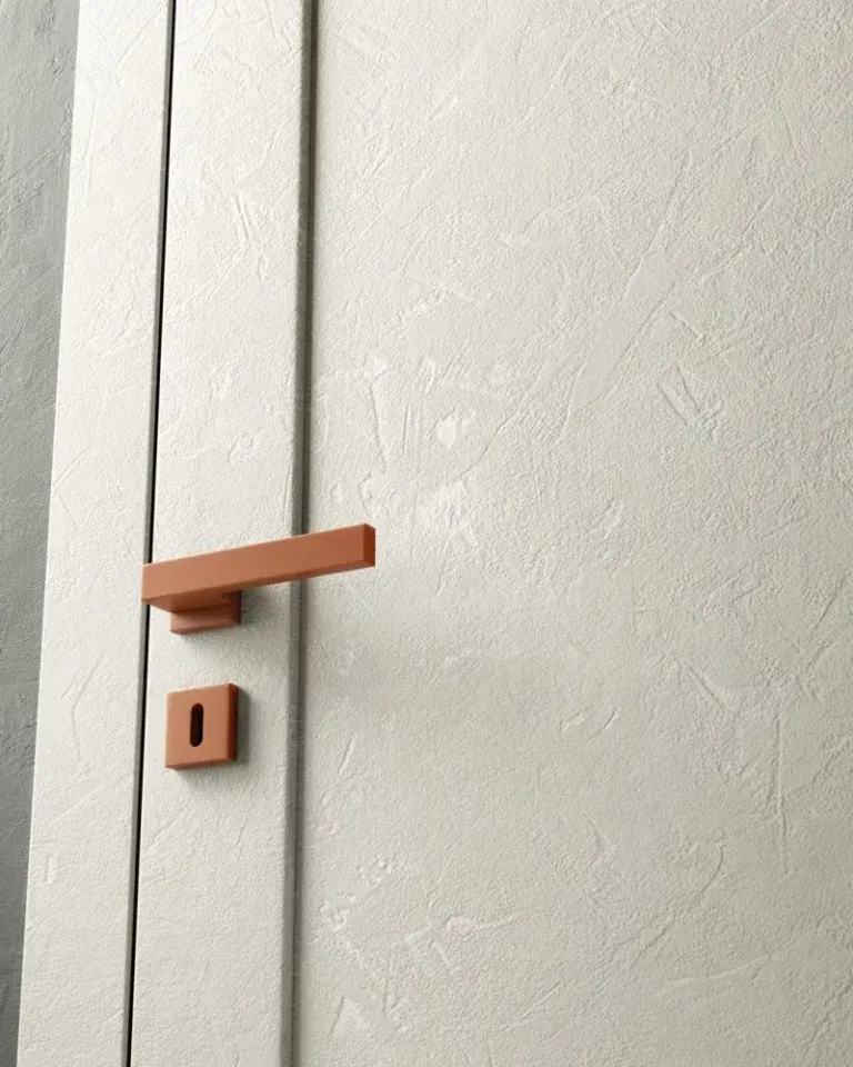 Primo piano di una porta color crema con finitura testurizzata, maniglia rettangolare color terracotta e placca della serratura abbinata.