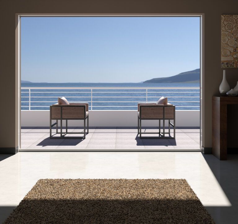 Un luminoso soggiorno con una grande finestra con vista sul mare, due sedie sono sistemate sul balcone.