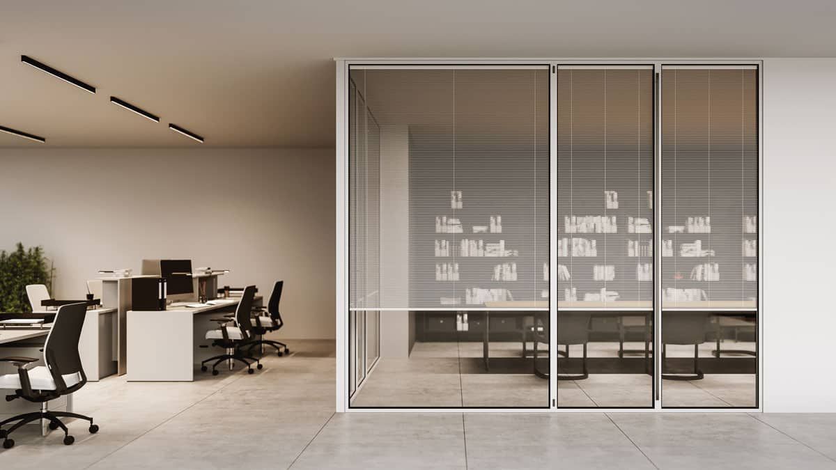 Spazio ufficio con sale riunioni con pareti in vetro, tende e scrivanie con computer. La luce del sole illumina l'area di lavoro.