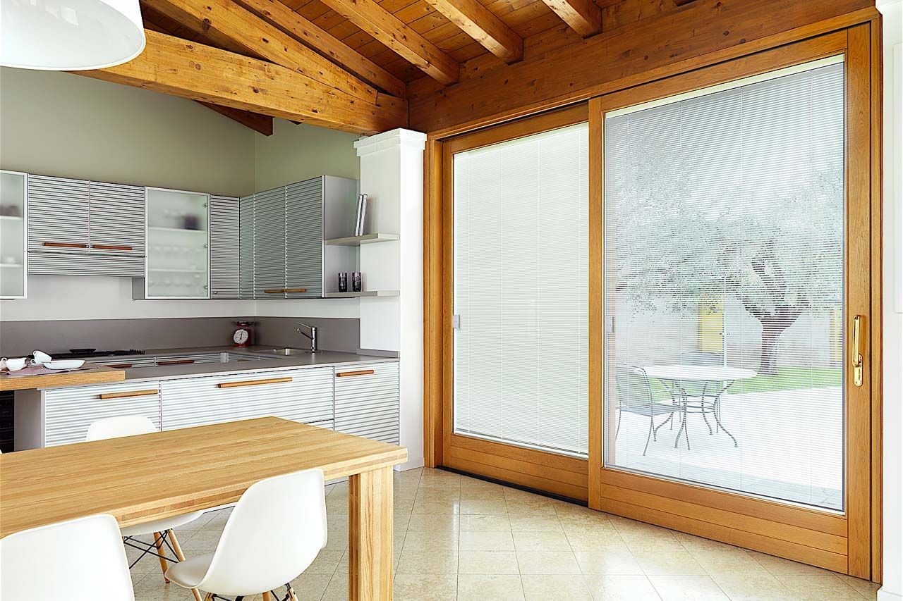 Una cucina luminosa con tavolo e sedie in legno, mobili bianchi e una grande porta scorrevole in vetro.