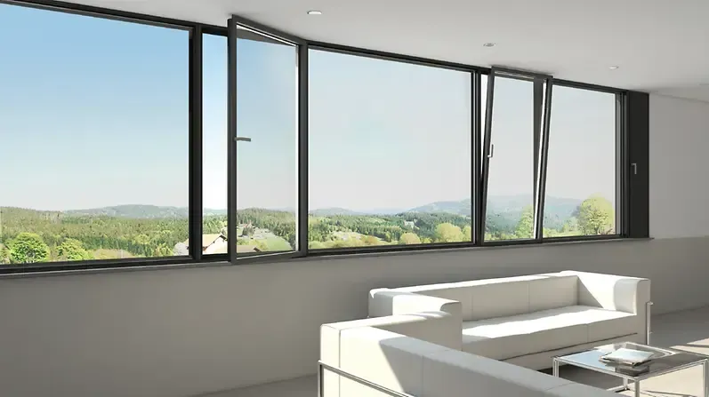 Soggiorno moderno con ampie finestre che si affacciano su un paesaggio verde. Due finestre sono parzialmente apribili. All'interno della stanza sono presenti divani bianchi e un tavolino da caffè.