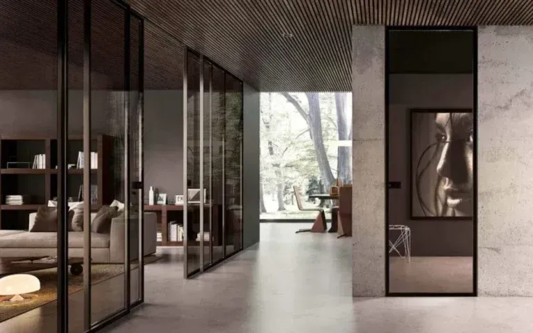 Moderno corridoio interno con porte scorrevoli in vetro, un quadro e vista sugli alberi. Pareti e pavimento sono in colori neutri.