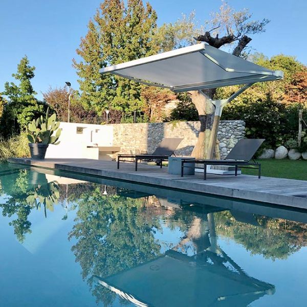 Scena di piscina con struttura ombreggiante a sbalzo, due sedie a sdraio e paesaggio.