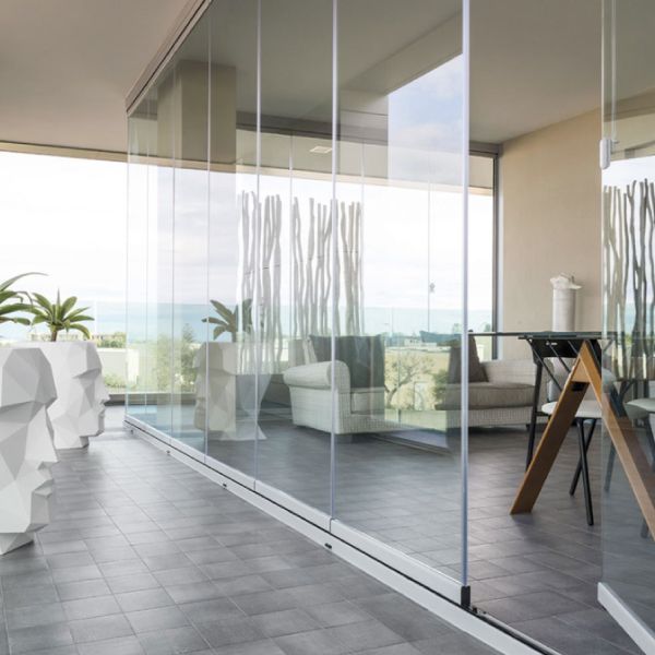 Balcone con pareti in vetro e vista sull'oceano. L'interno è caratterizzato da un divano bianco, un tavolo e fioriere decorative. Il pavimento è piastrellato.