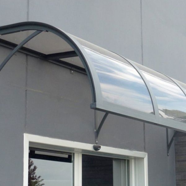 Una tettoia curva e trasparente sopra la porta di un edificio grigio. Sono visibili la struttura metallica e i supporti.