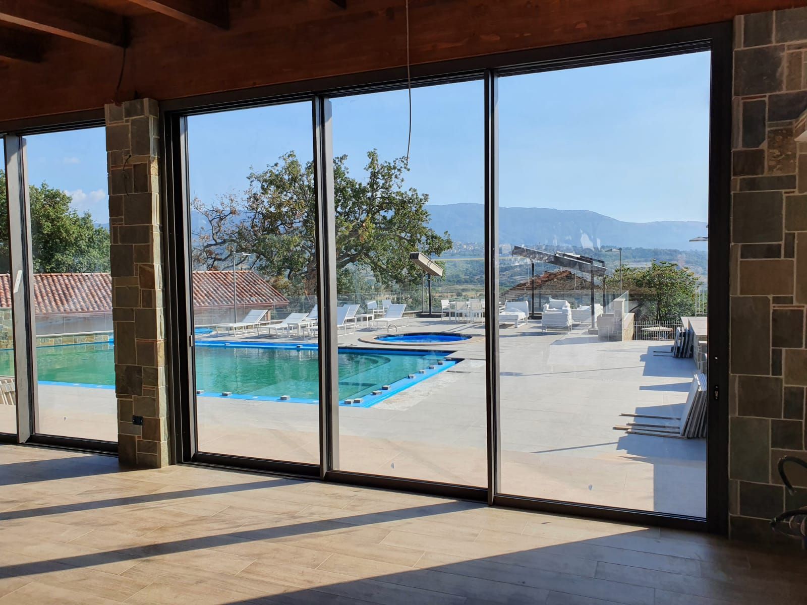 Soggiorno con ampie finestre che si affacciano su un cortile verde. Una poltrona in pelle e un pouf sono appoggiati su un tappeto scuro davanti alle finestre.