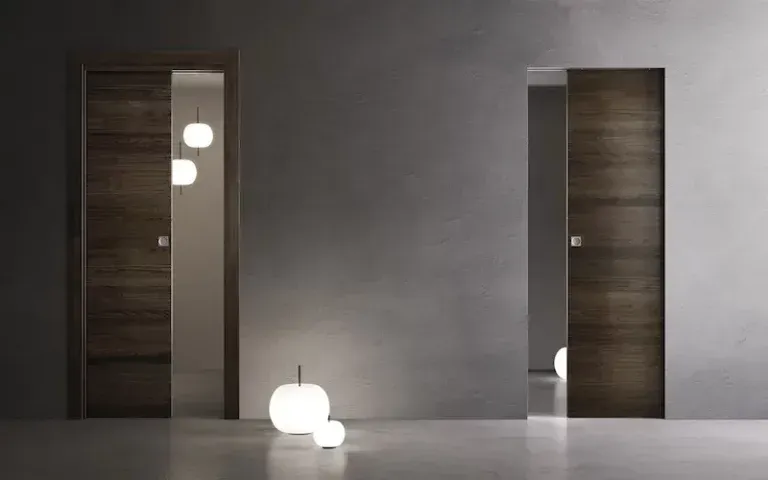 Due moderne porte a scomparsa in legno inserite in un interno minimalista grigio con luci soffuse.