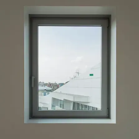 Cornice di una finestra con vista sul tetto di un edificio bianco e sullo skyline della città contro un cielo azzurro pallido.