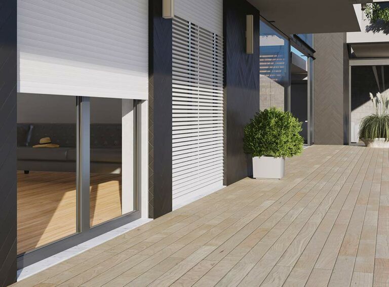 Vista esterna di un edificio moderno con persiane bianche, una terrazza in legno e una pianta in vaso.