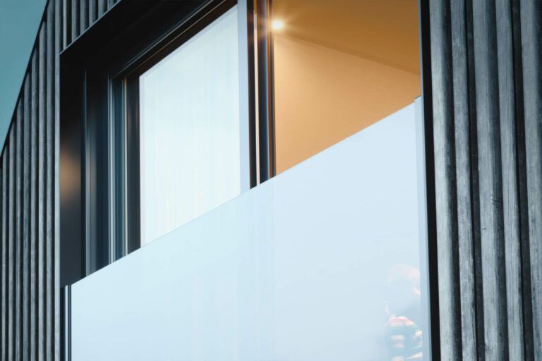 Vista esterna di un edificio moderno con finestra. Le caratteristiche principali includono un pannello bianco, un rivestimento verticale scuro e una calda illuminazione interna.