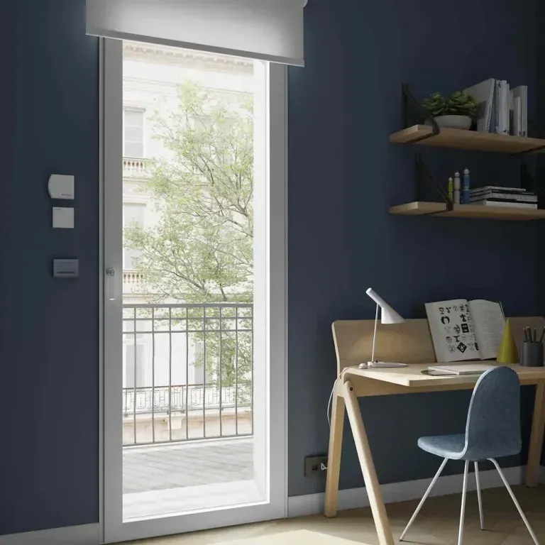 Stanza con pareti blu e una grande porta che conduce a un balcone. Vicino alla porta ci sono una scrivania e una sedia.