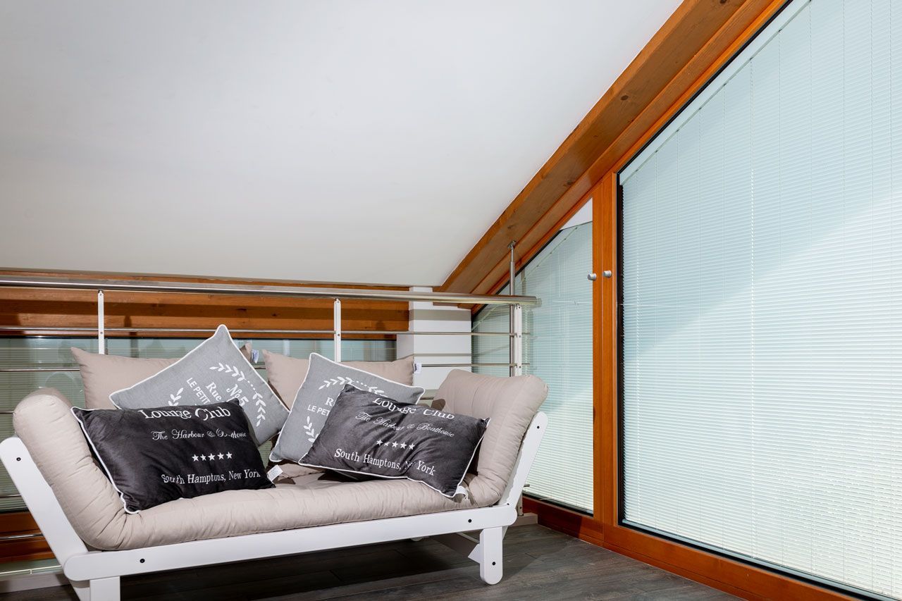 Un piccolo divano futon bianco con cuscini grigi è posizionato accanto a una grande finestra in un loft.