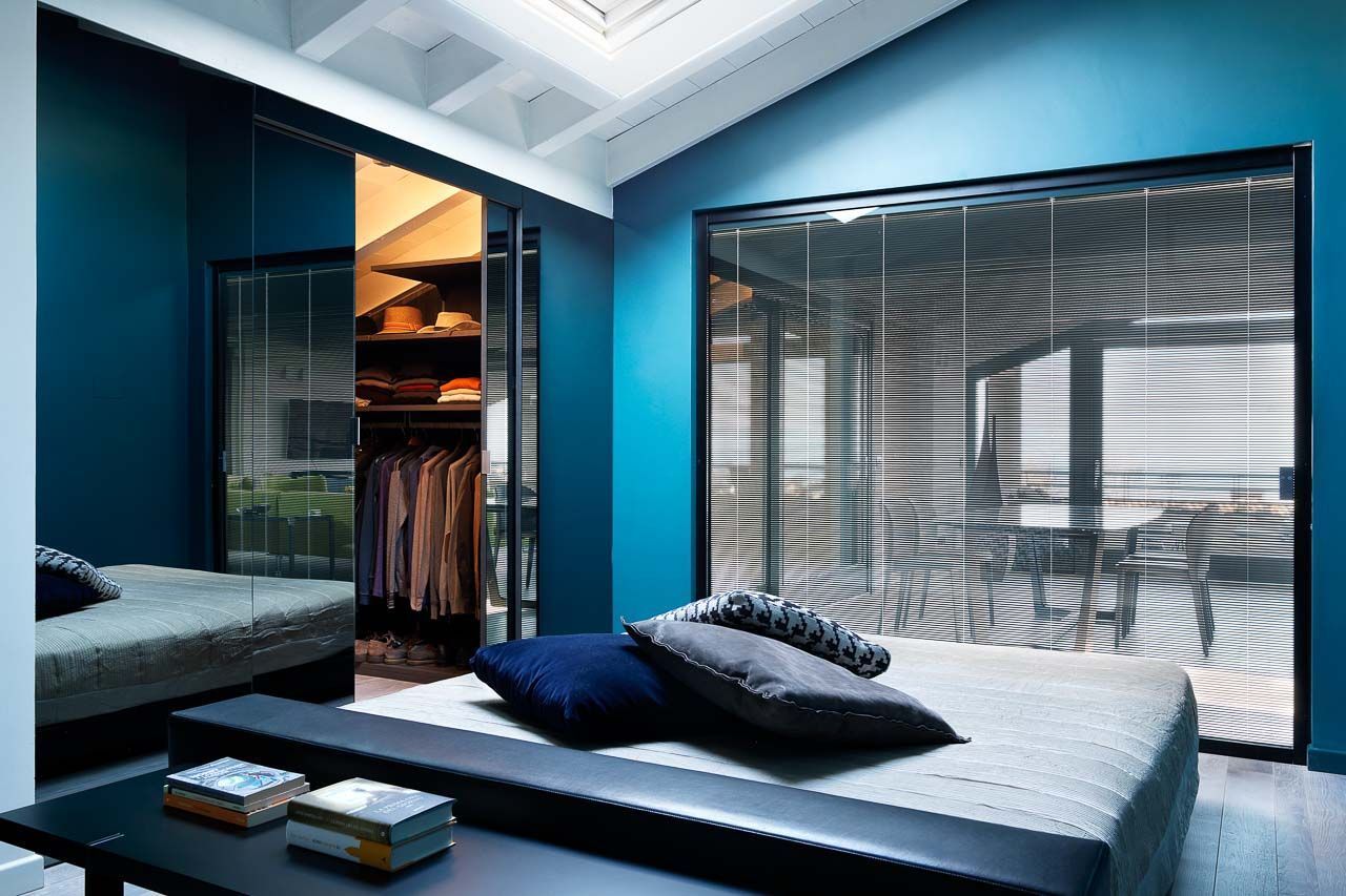 Una camera da letto moderna con pareti color verde acqua, un letto basso e porte scorrevoli in vetro che conducono a una cabina armadio e a una vista sull'esterno.
