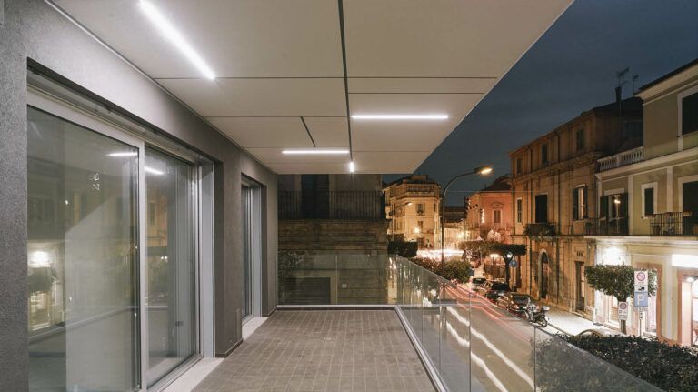 Balcone con vista sulla strada al tramonto, ringhiere in vetro, illuminazione moderna e vista sugli edifici.