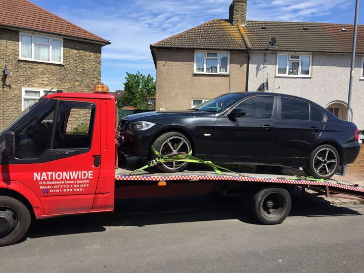 A.C Recovery's, 24 hour towing service in Barking and Dagenham,  black car being towed by a red towing truck in broad daylight