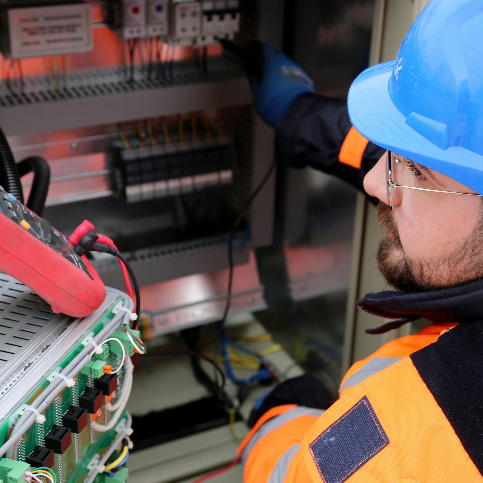 Electrician in blue helmet and gloves wiring electrical cables in a white wall.